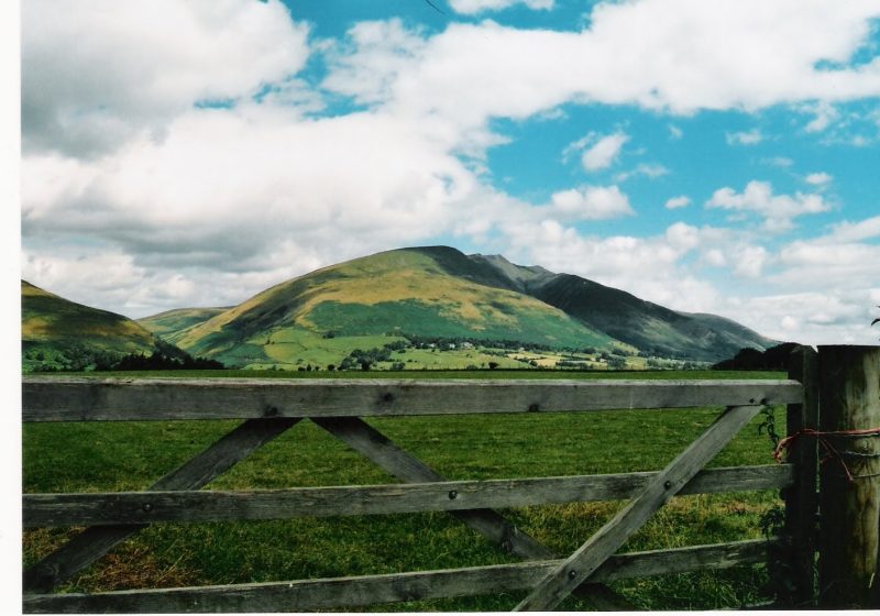 Green hills beyond a wooden field gate, bright cloud overhead