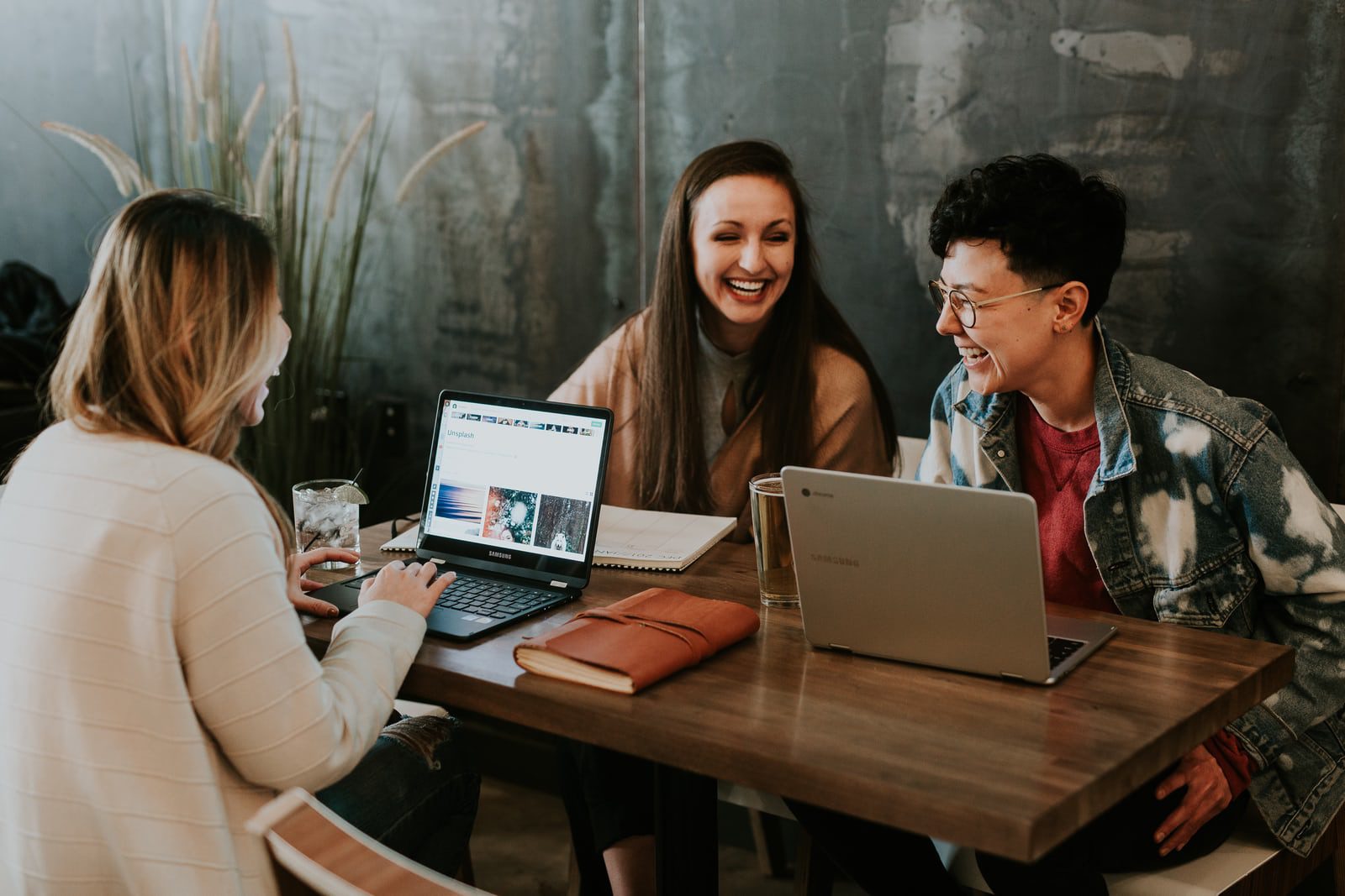 Three people laughing round a cafe table with laptops open