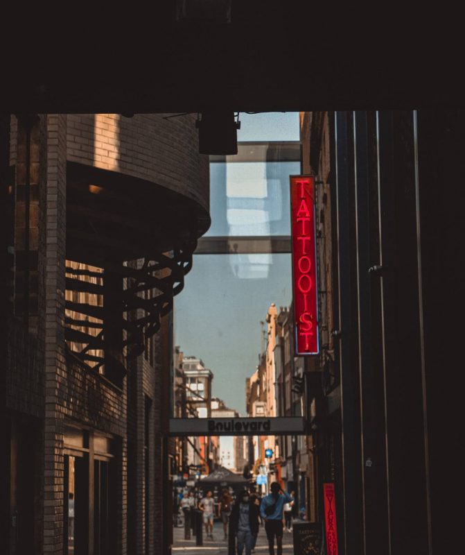 A narrow city street seen through an arch, a red neon sign on the wall