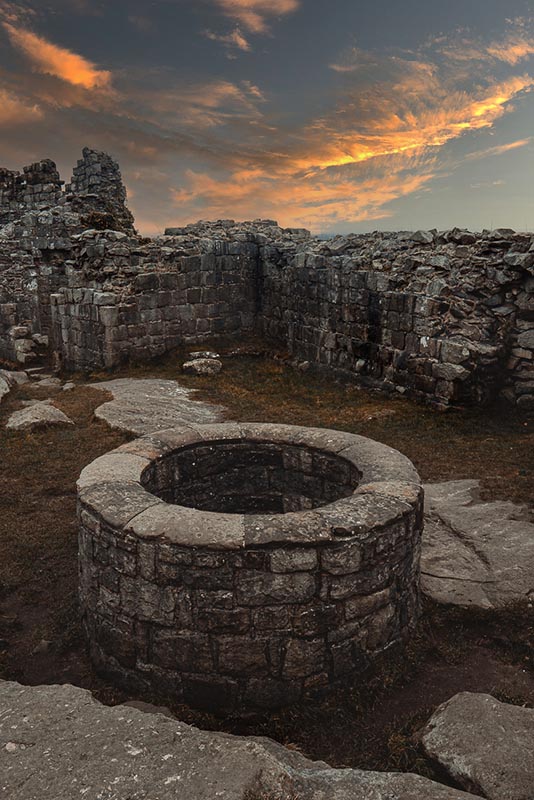A stone well inside a ruined building, sunset cloud above the broken walls