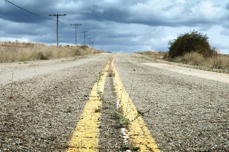 An empty road running to the horizon across flat scrub under a big sky