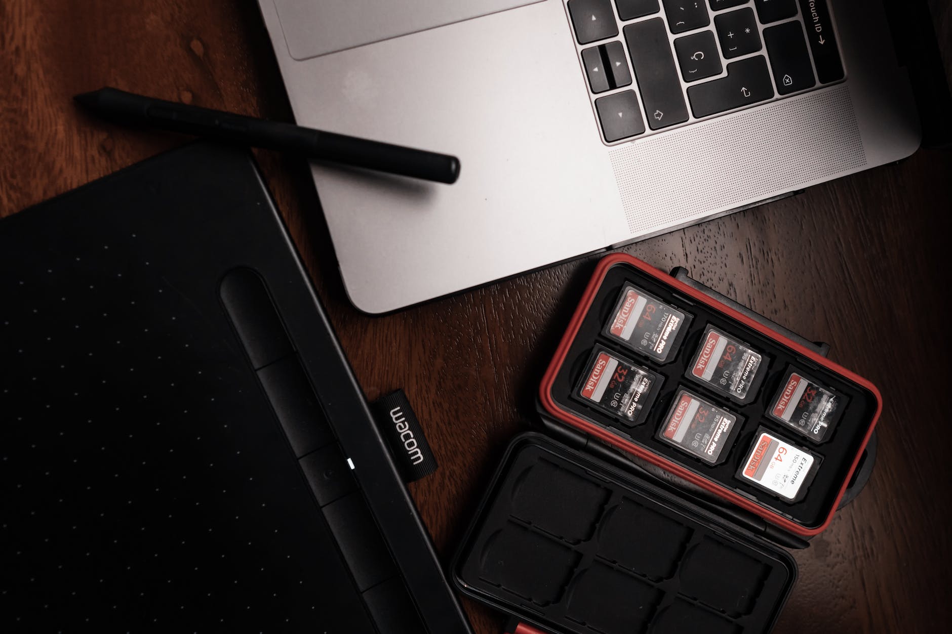 A laptop, graphics tablet and a case of memory cards on a dark desk