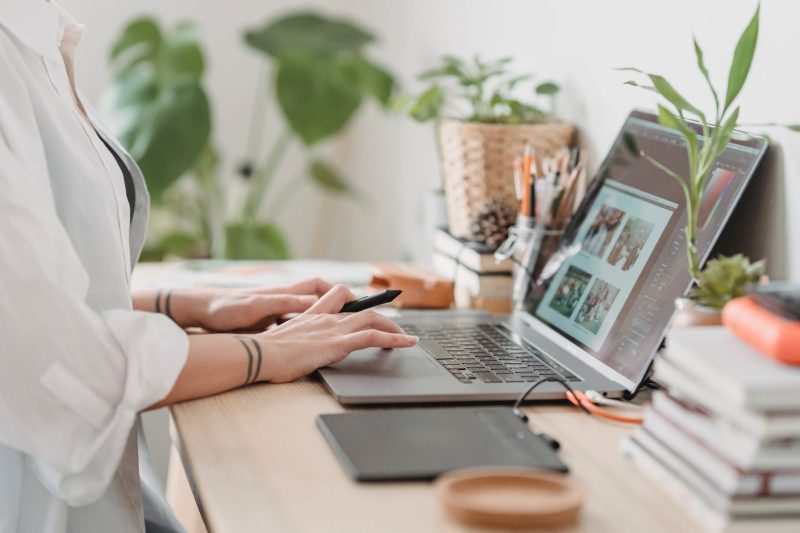Someone working at a laptop at a bright desk with plants and notebooks