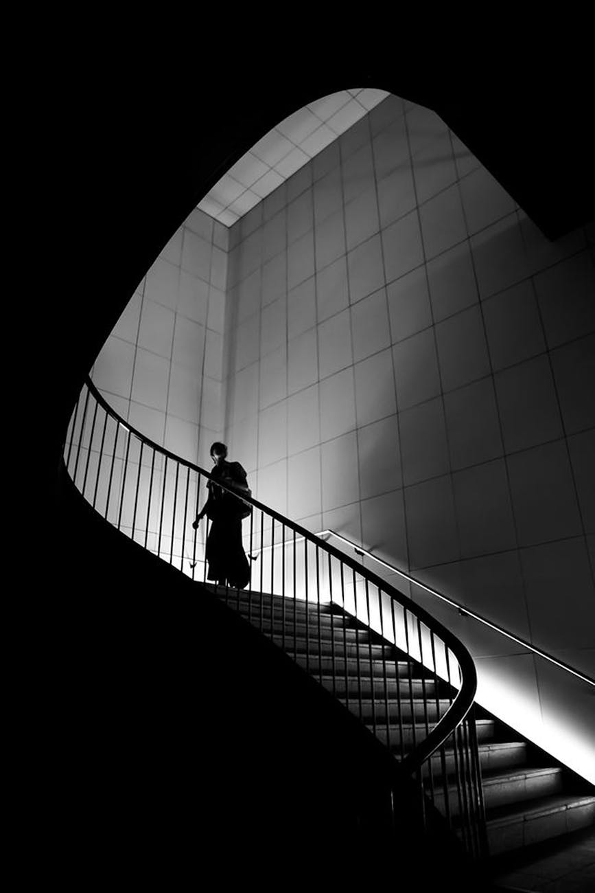 a black and white photo of a person going up a spiral staircase