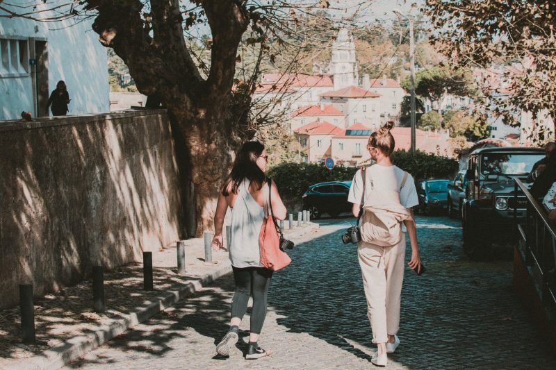 two female photographers walking down a street on a sunny day