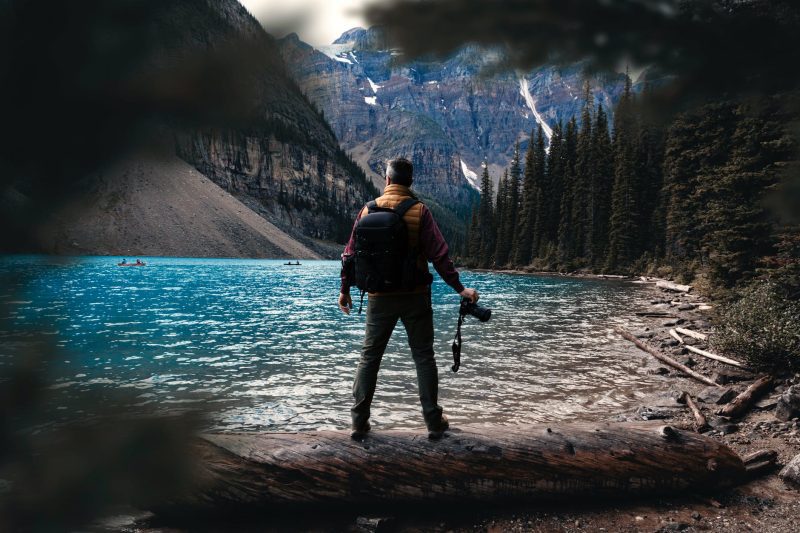a photographer stood at the edge of a lake on a fallen tree trunk