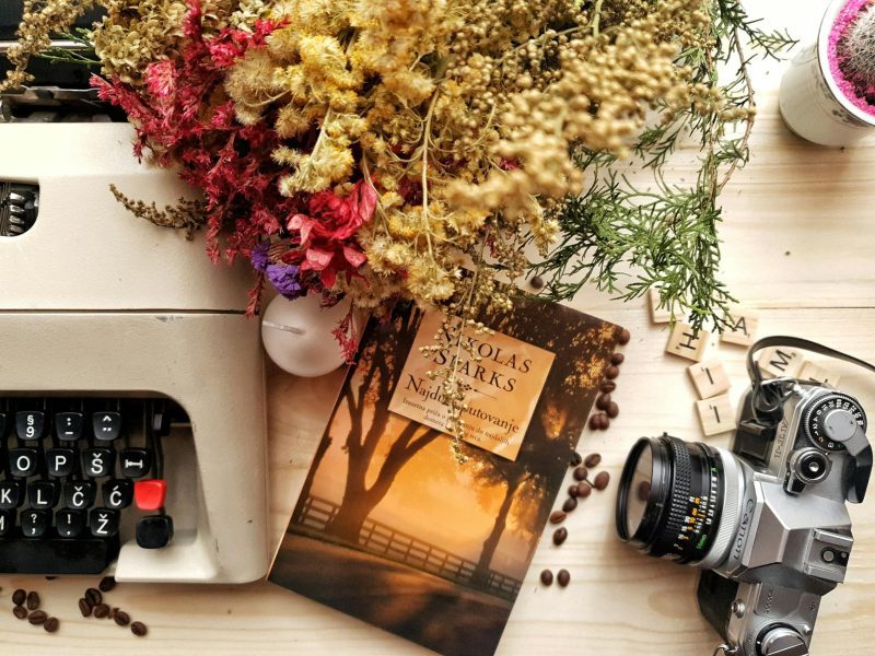 overhead photo of a typewriter, flowers, book and old film camera