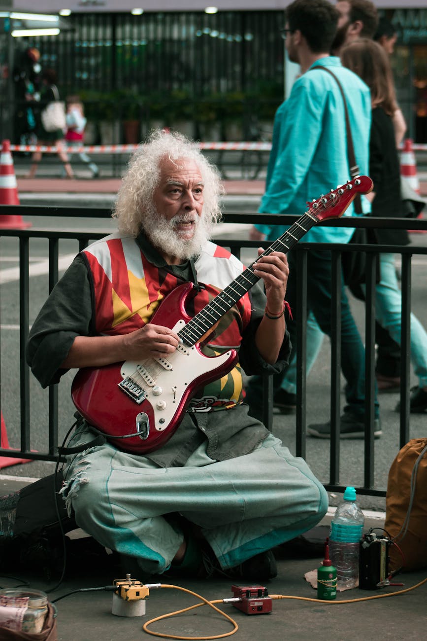 A street busker playing electric guitar on the street sat down