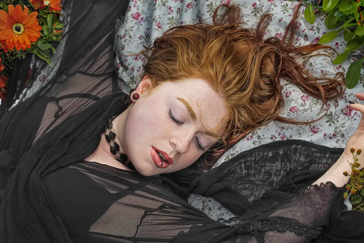 A red-haired woman lying among flowers with her eyes closed