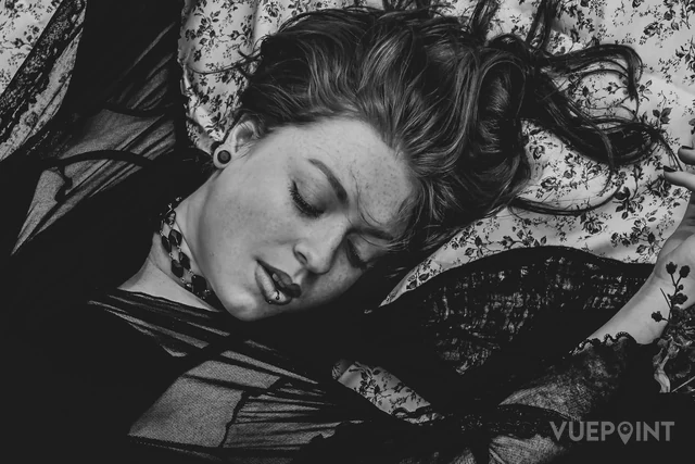 A woman asleep among lace and patterned fabric, in black and white