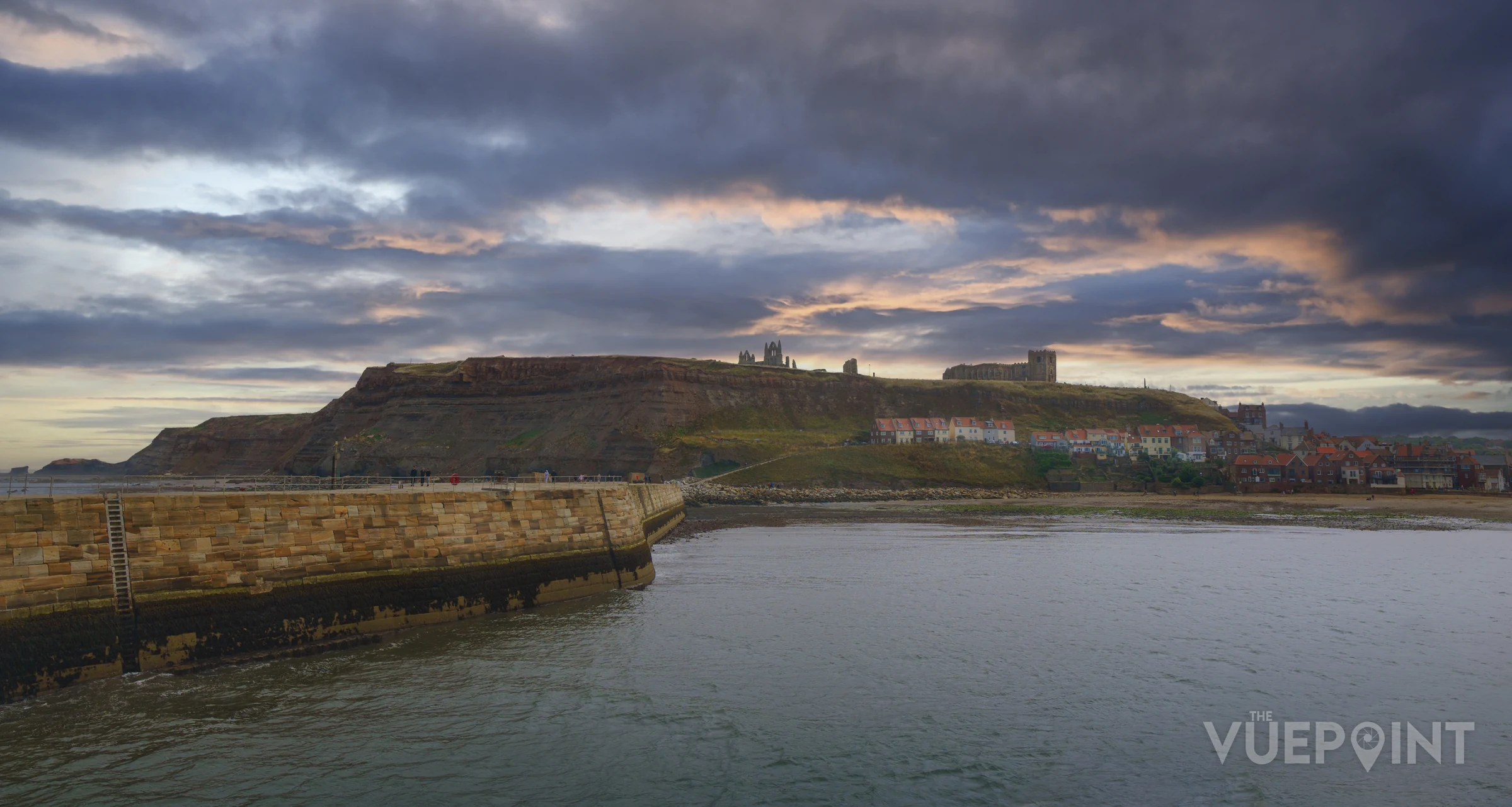A harbour wall and the town beyond under a heavy sky