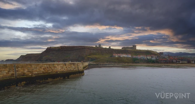 A harbour wall and the town beyond under a heavy sky