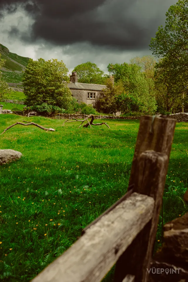 A wet green field and a wooden fence, a cottage beyond