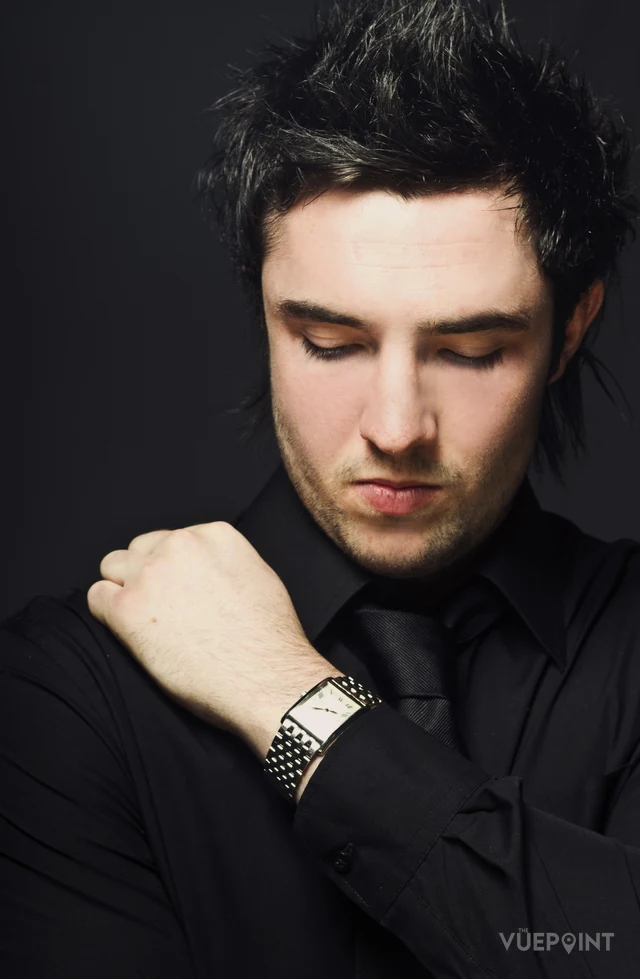 A young man in black, head lowered, studio light