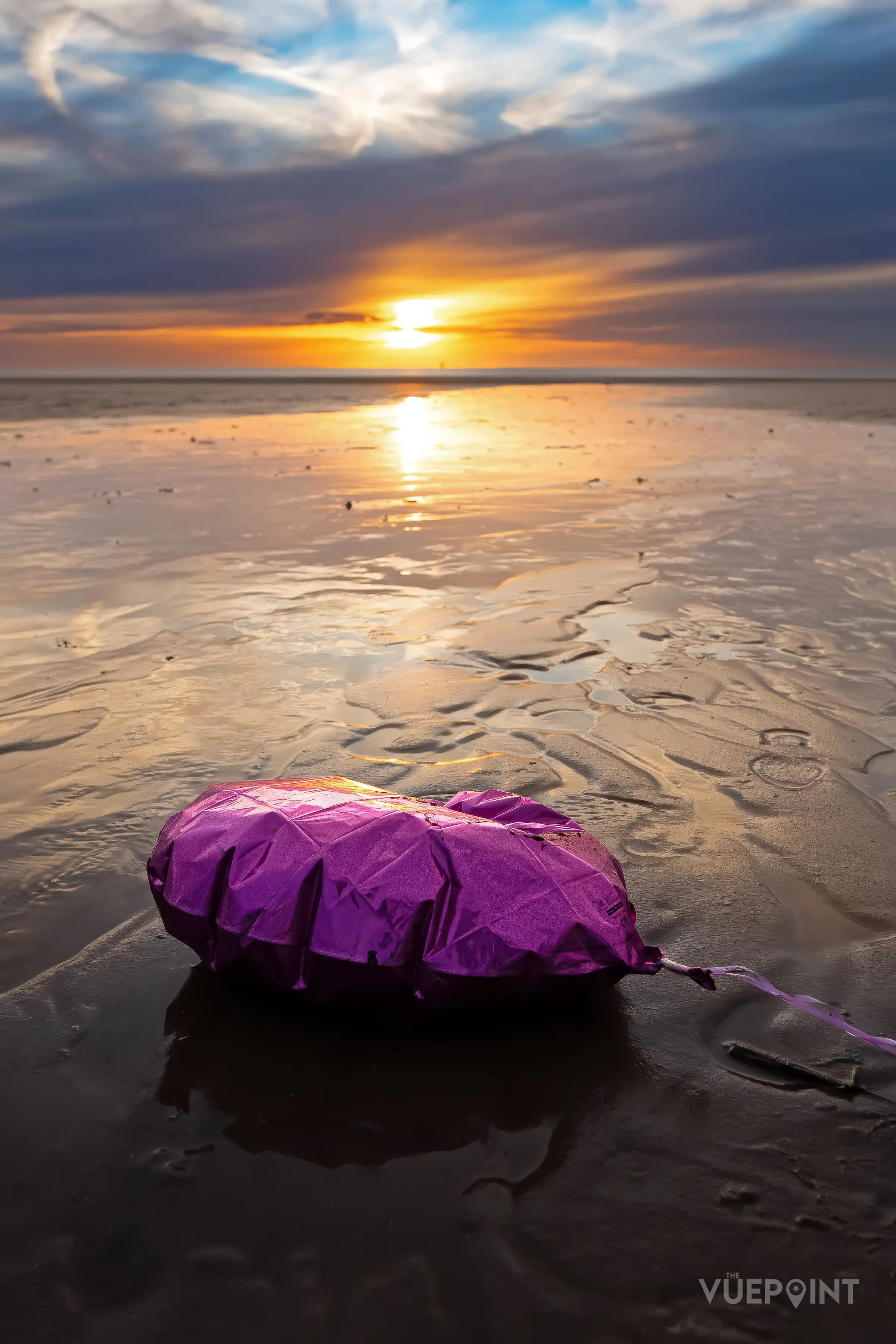 A pink heart-shaped balloon lying on wet sand at sunset