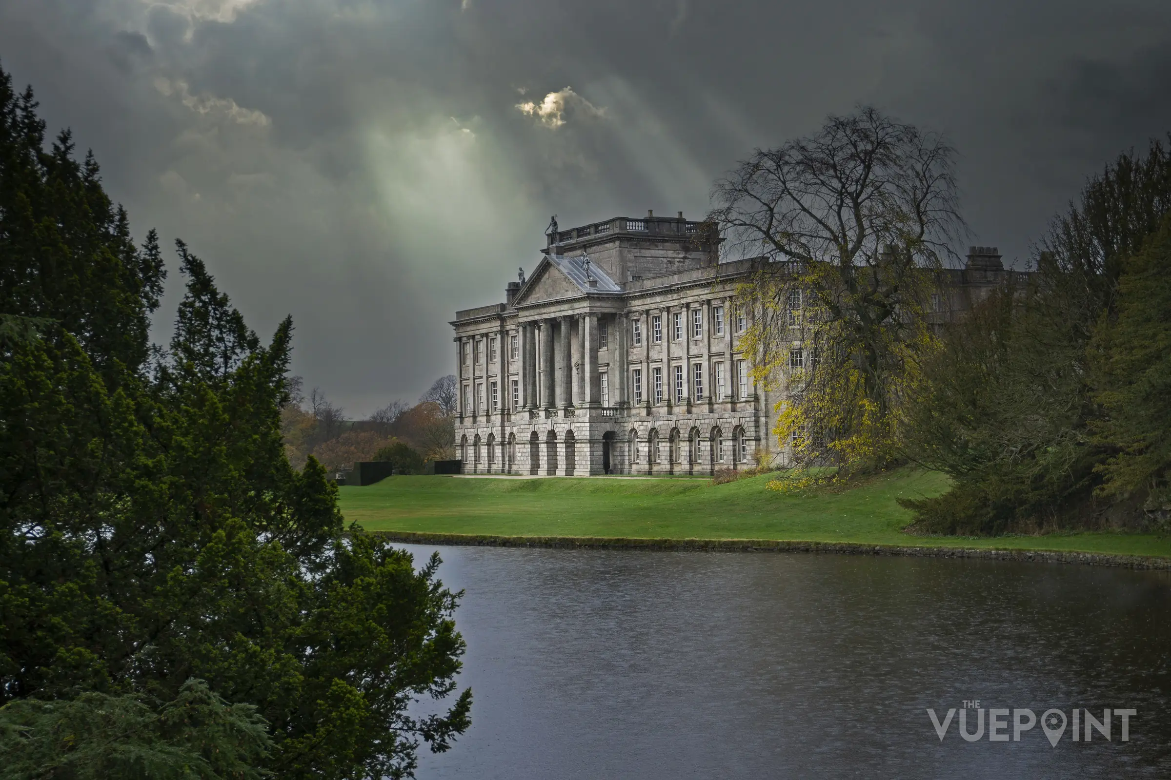 Sunlight breaking over a stately home and its lake
