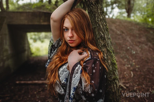 A woman with long red hair leaning against a tree