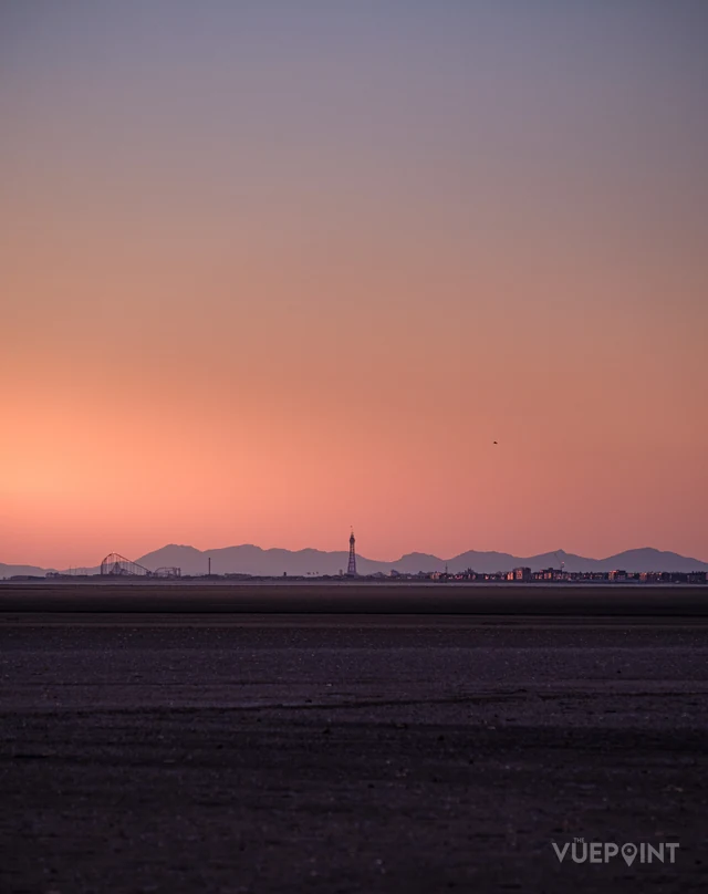 A pink dawn over flat wet sand, the coast a thin line on the horizon