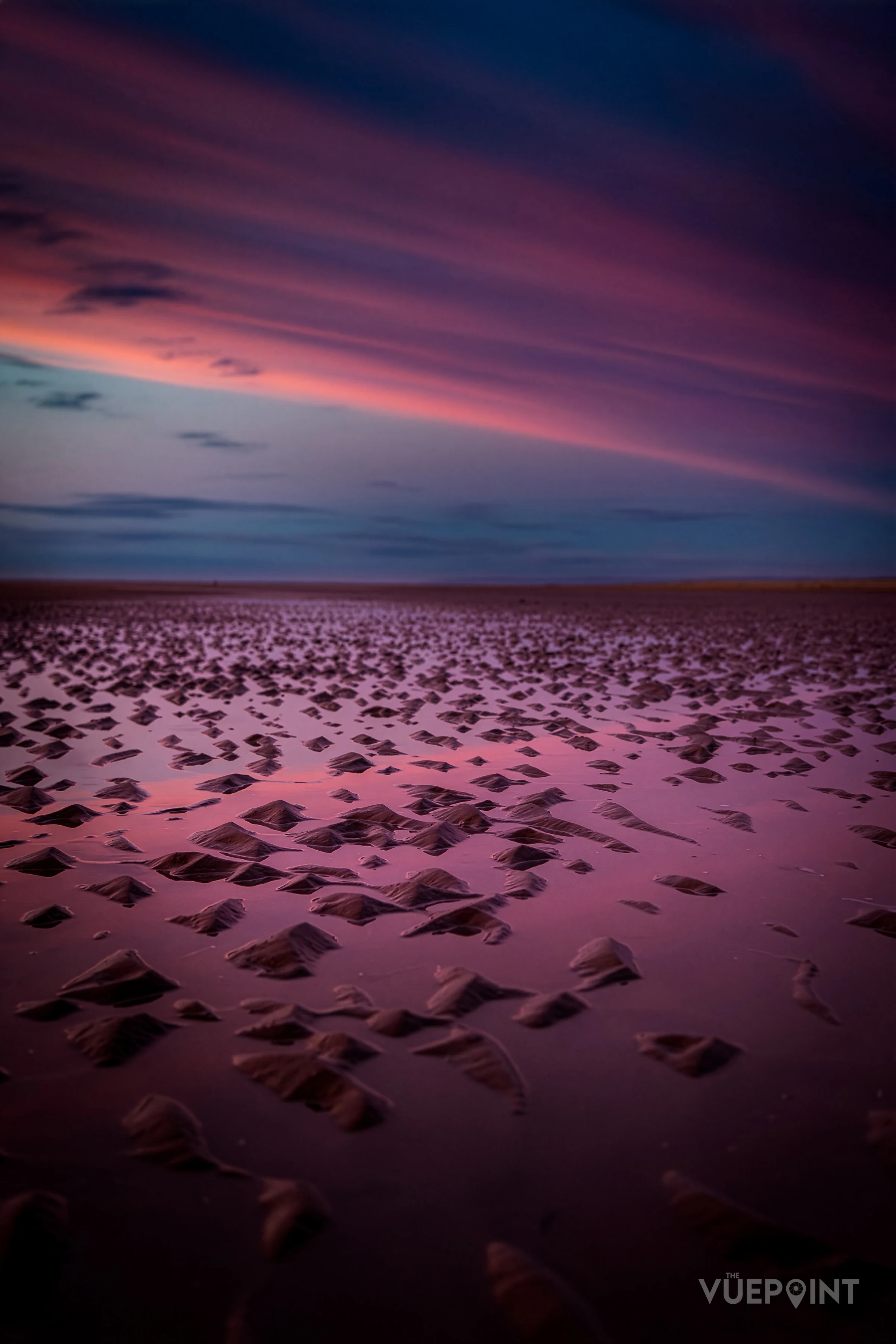 Ripples in wet sand under a pink and purple sky