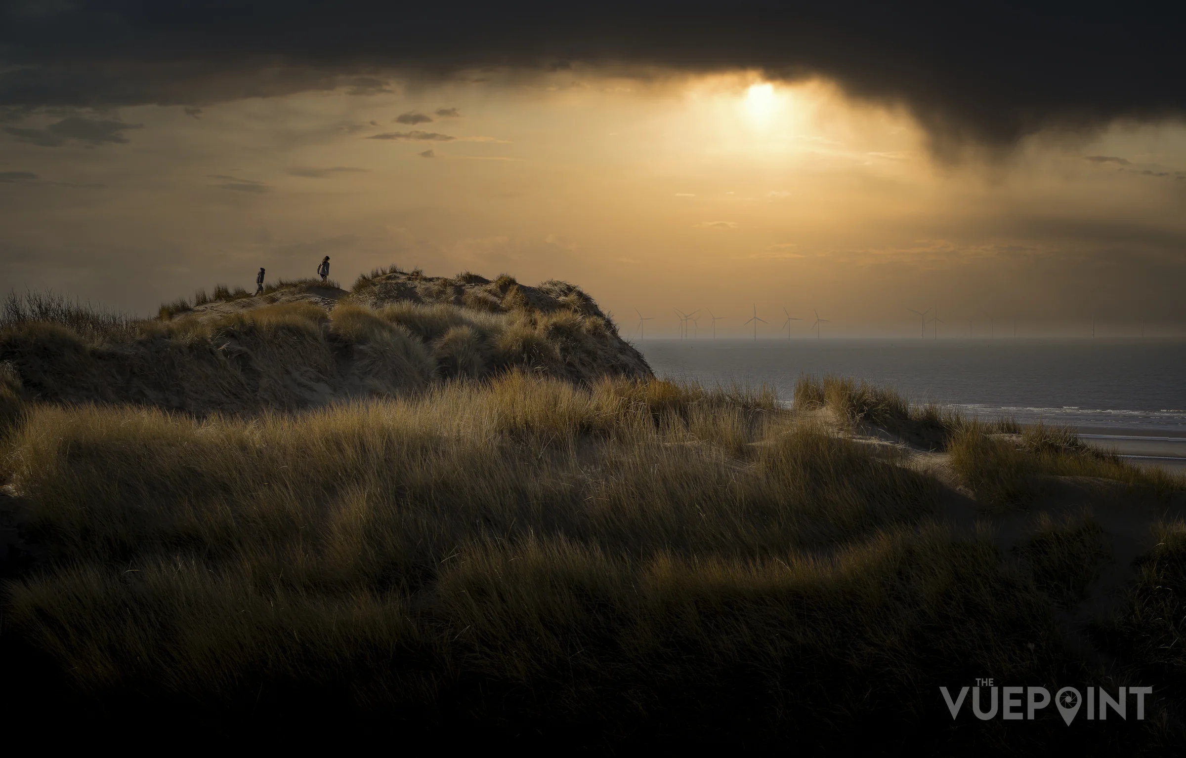 The sun breaking through heavy cloud over the dunes