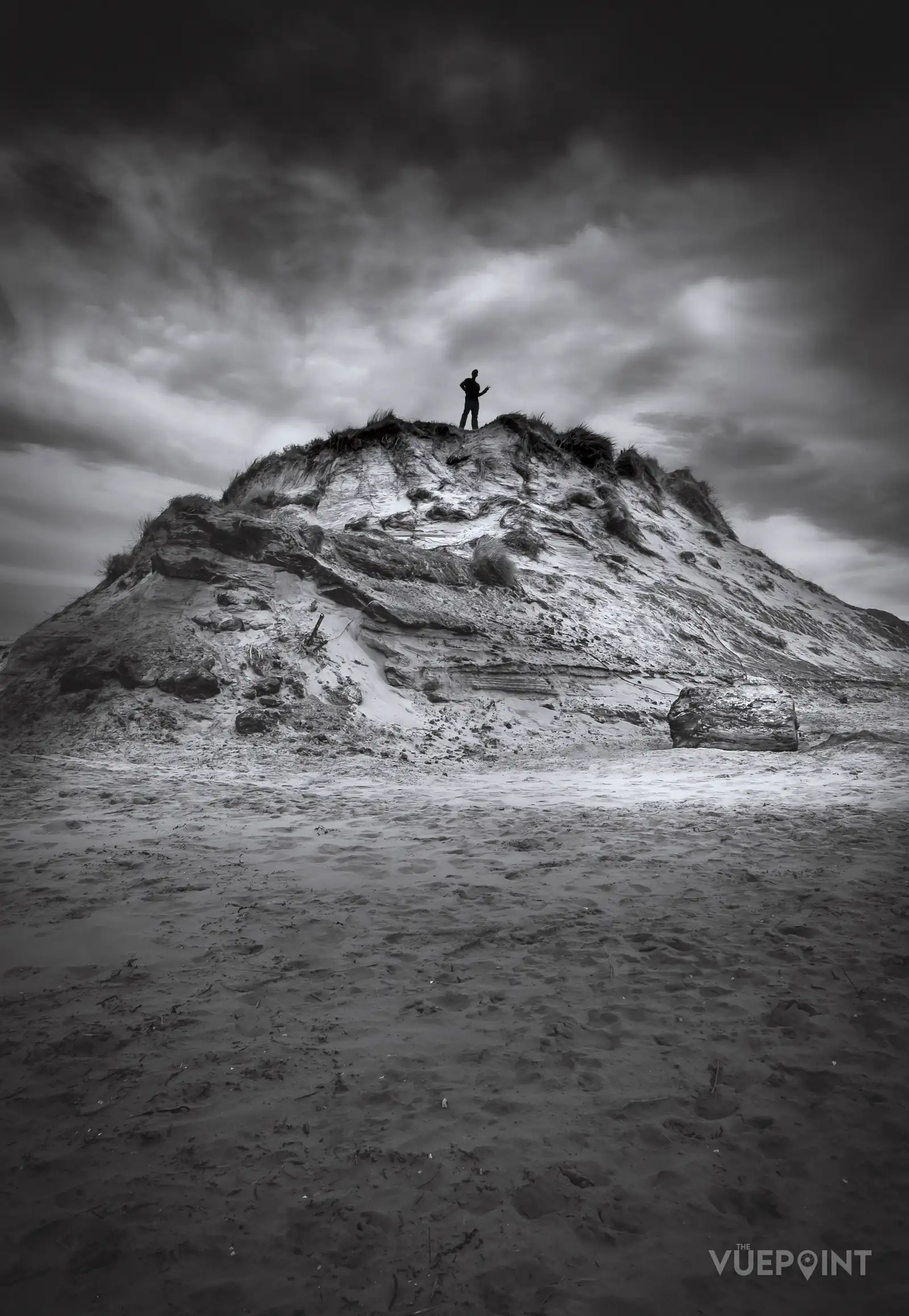 A figure standing on the summit of a sand dune, in black and white