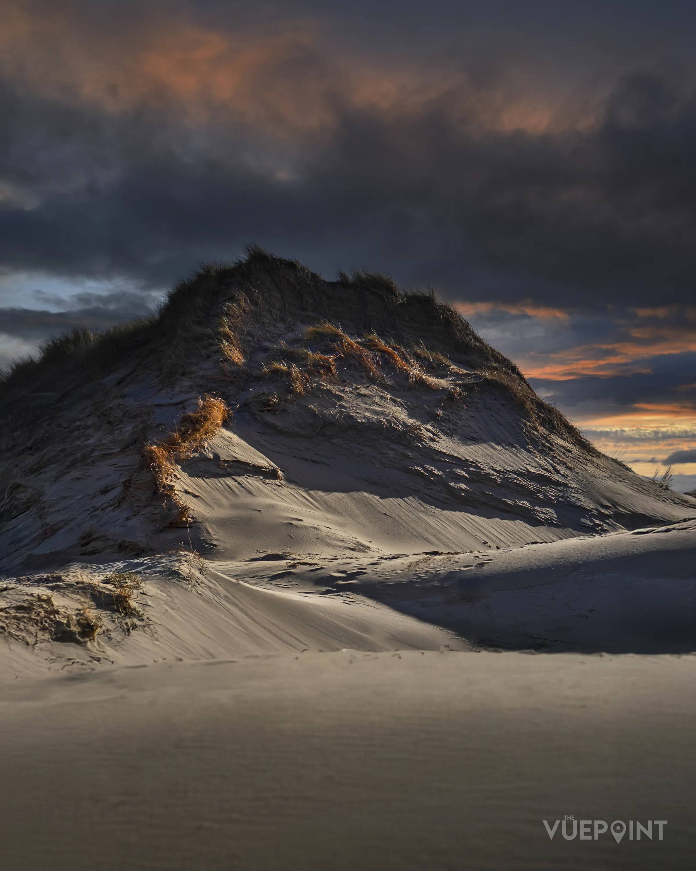 A large sand dune under a broken evening sky