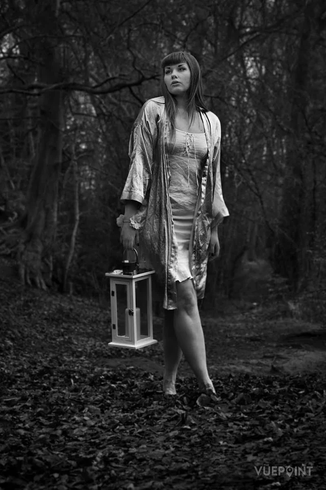 A woman carrying a lantern in dark woodland, in black and white