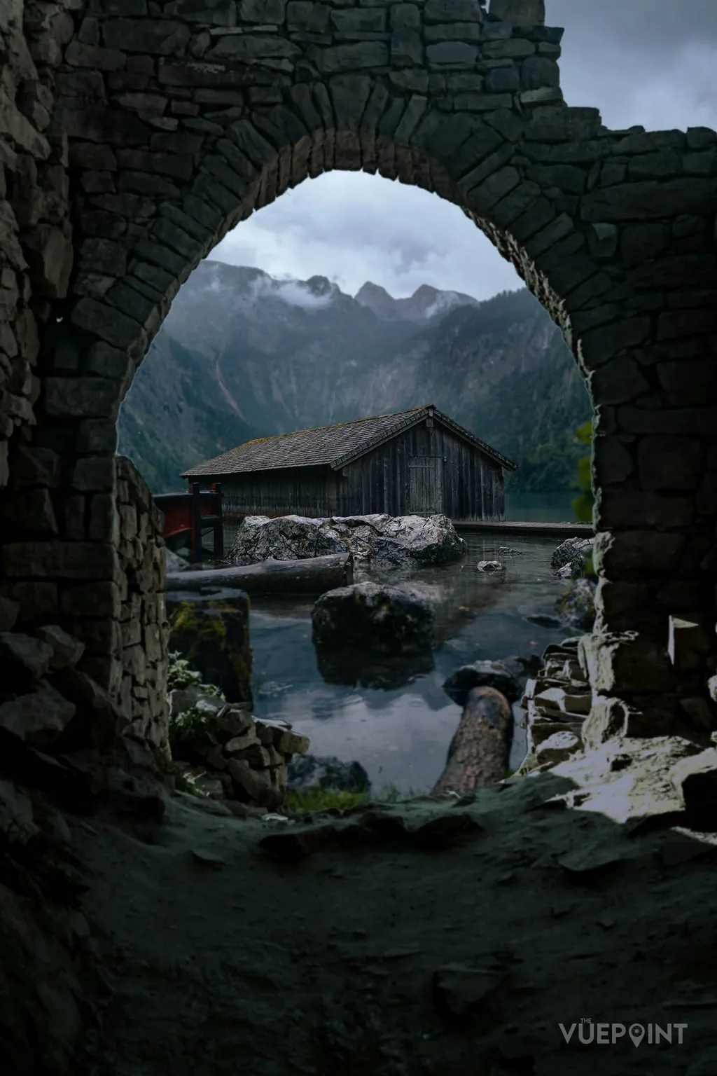 Mountains and a wooden hut seen through a ruined stone arch
