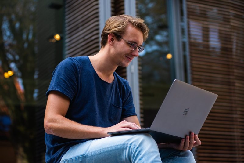 a man sat outdoors with an apple macbook on his lap