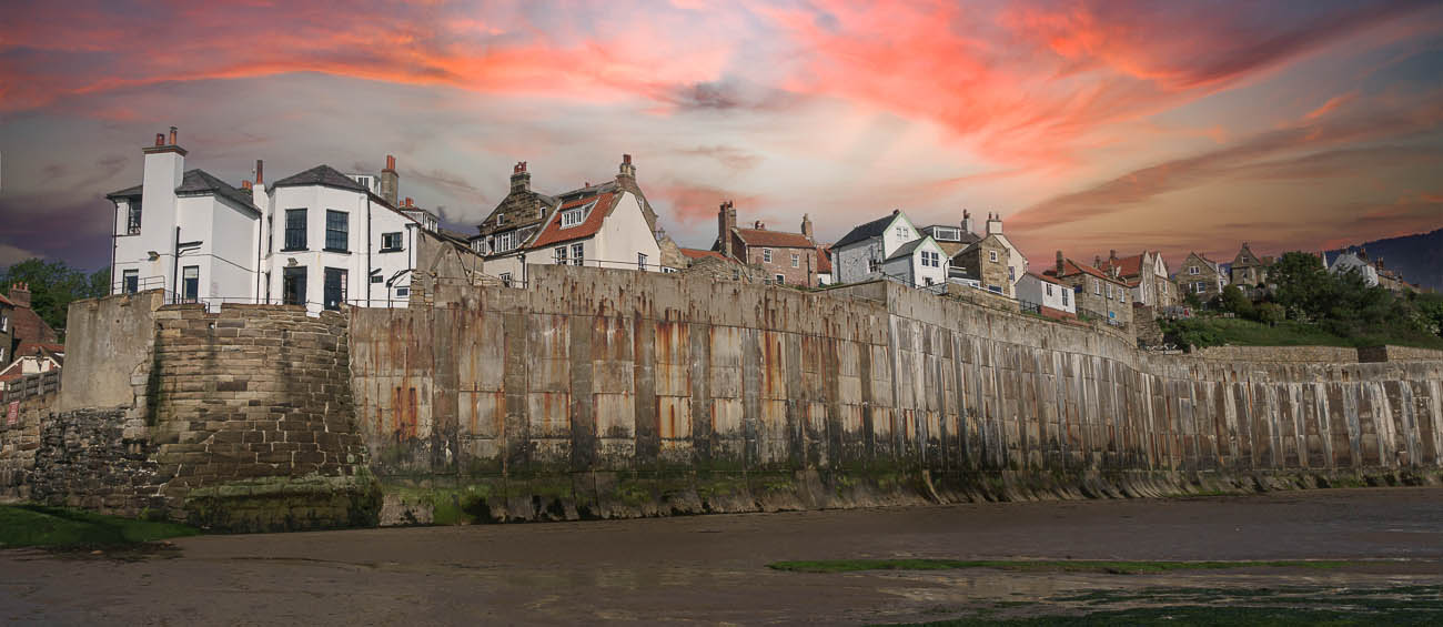 Robin Hood's Bay in Yorkshire looking at the houses which stand above the beach looking out at the sea. The sky is sunset