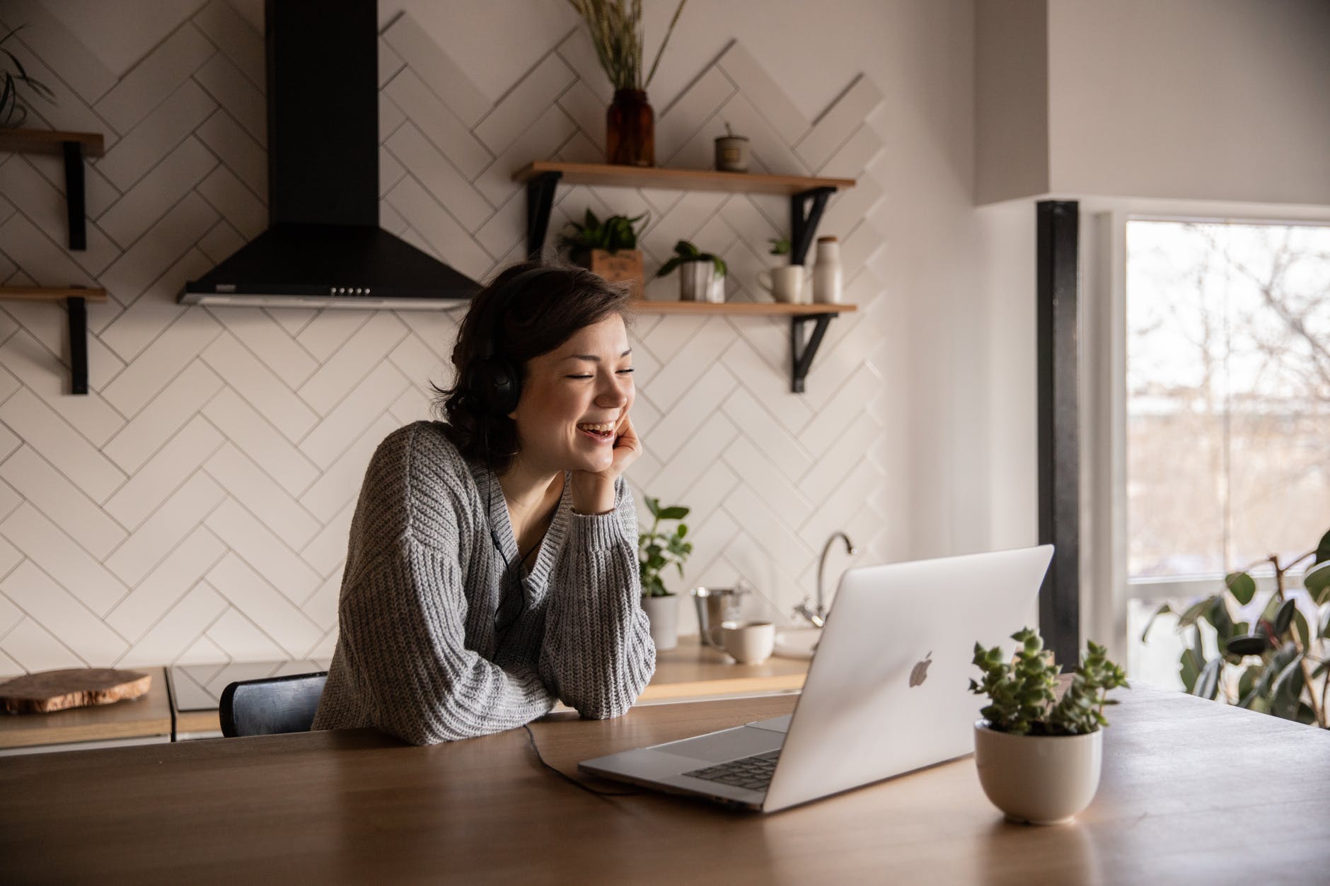 A lady smiling at her apple macbook laptop in her kitchen