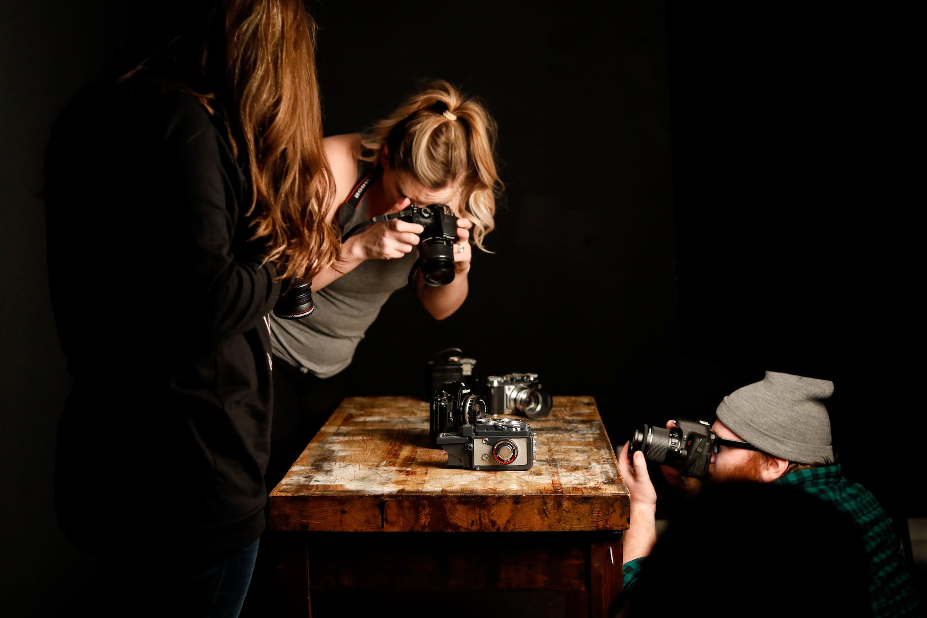 three photographers stood in a dark room taking photos of old camera on a wooden table