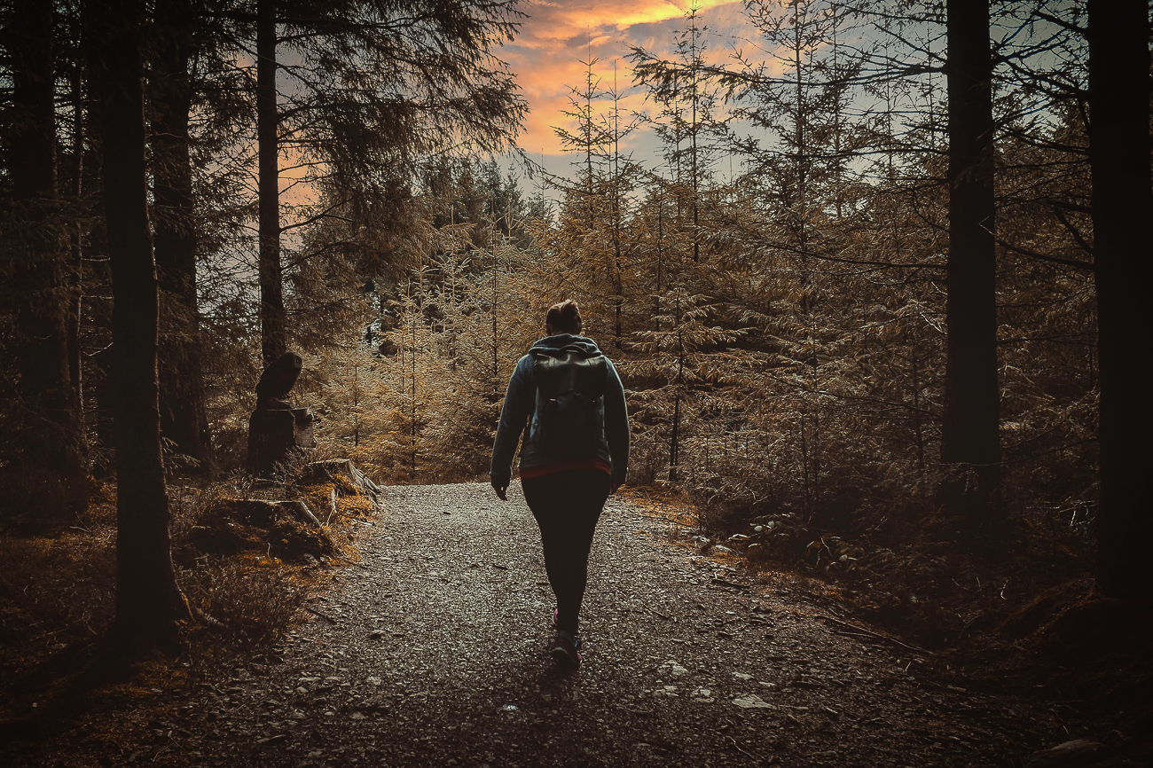 A woman walking through a woods on a stone path at sunset