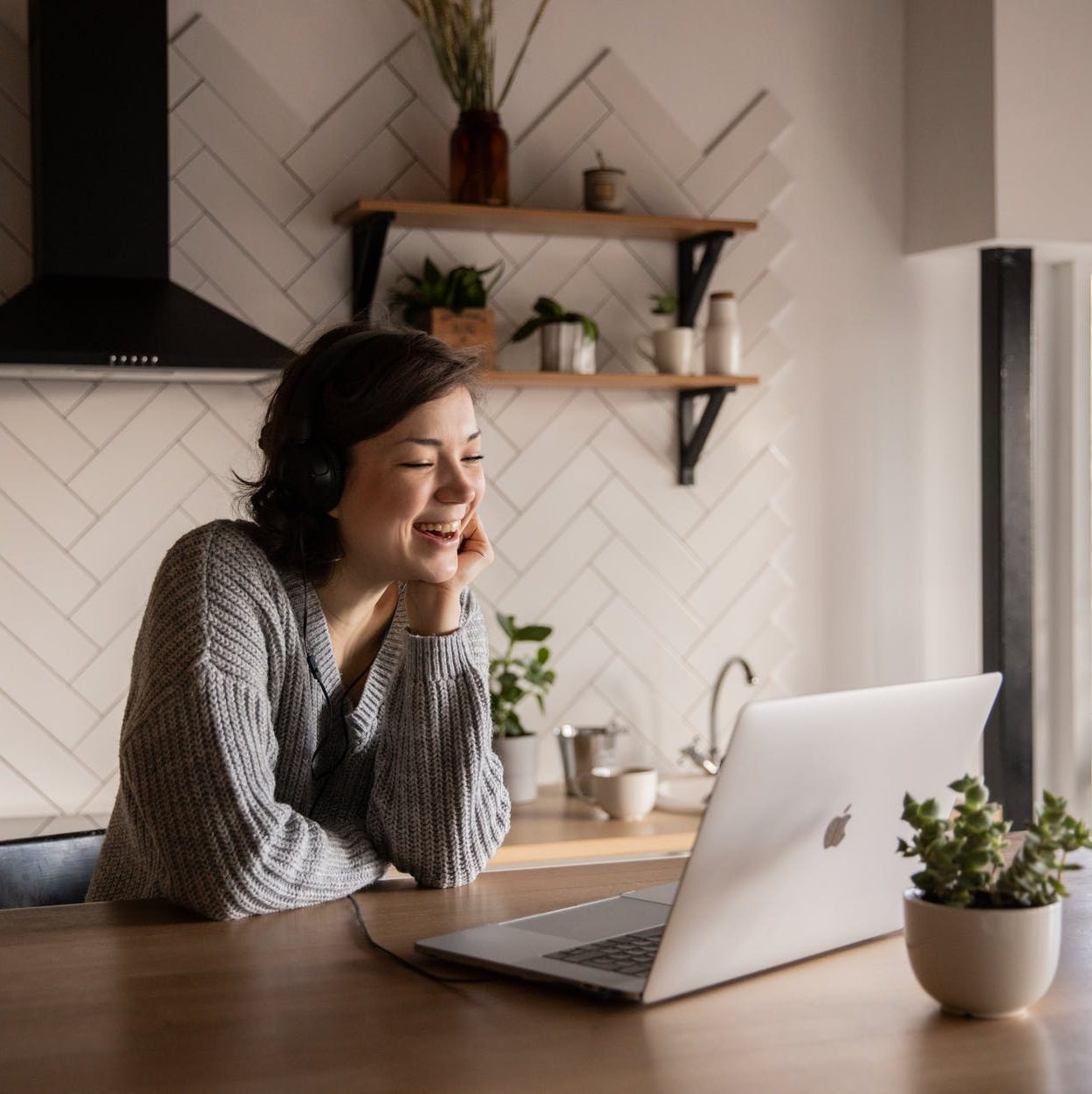 a smiling lady in a kitchen laughing at her apple imac laptop