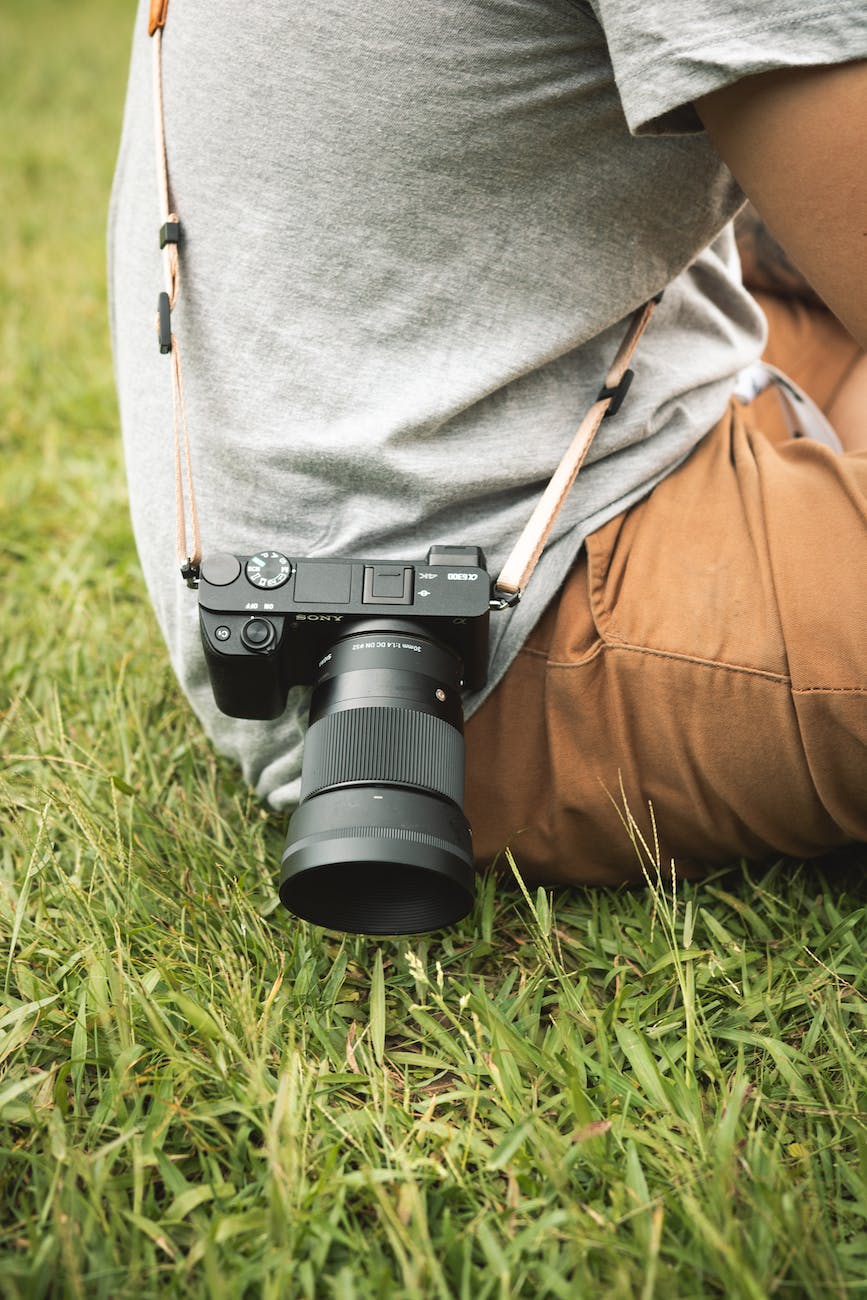 A camera on a strap around the body of a person sat on grass