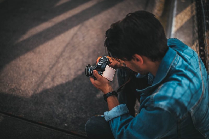 man sitting on pavement holding dslr camera