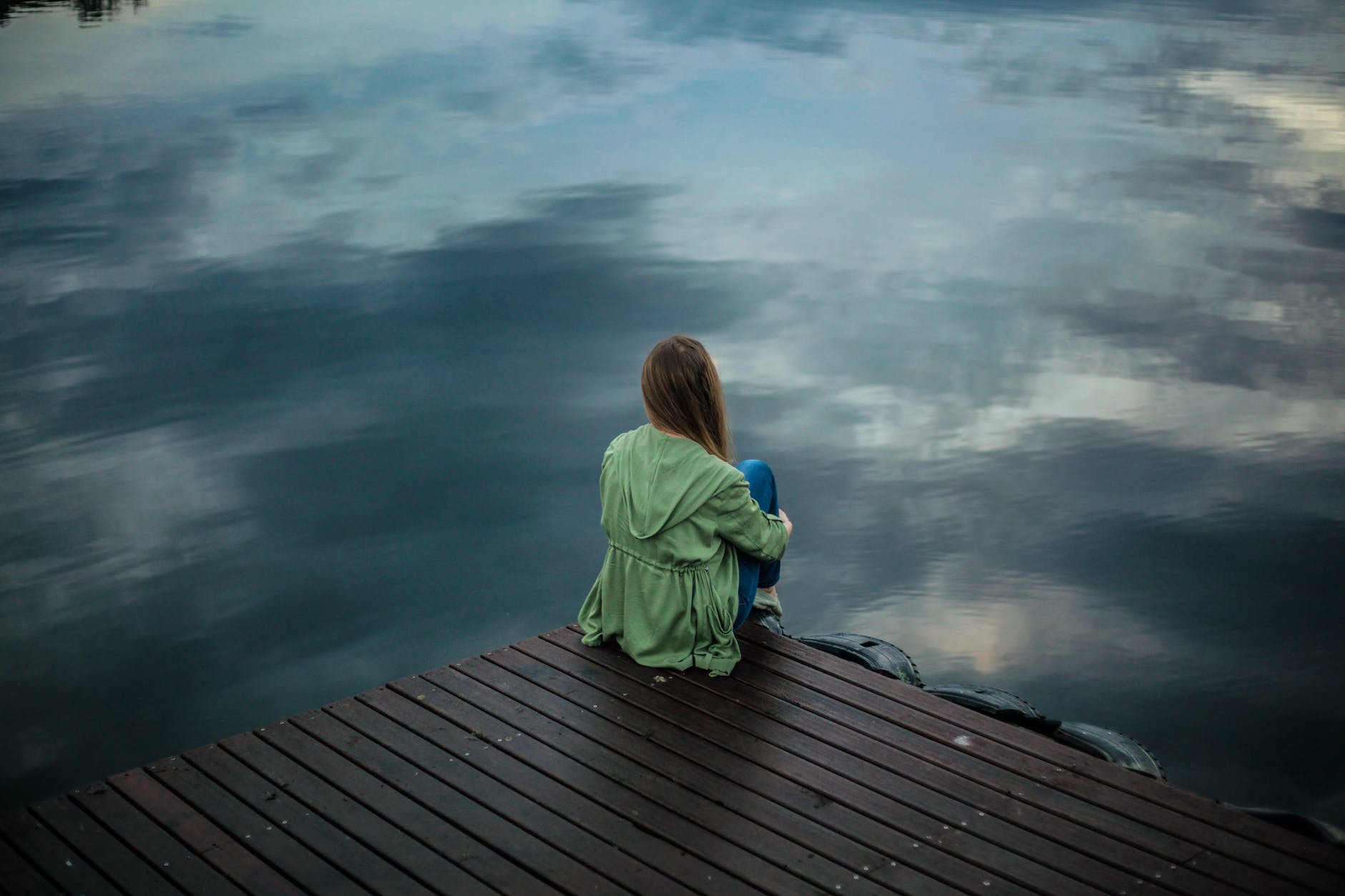 a lady sat on the edge of a jetty looking into the water