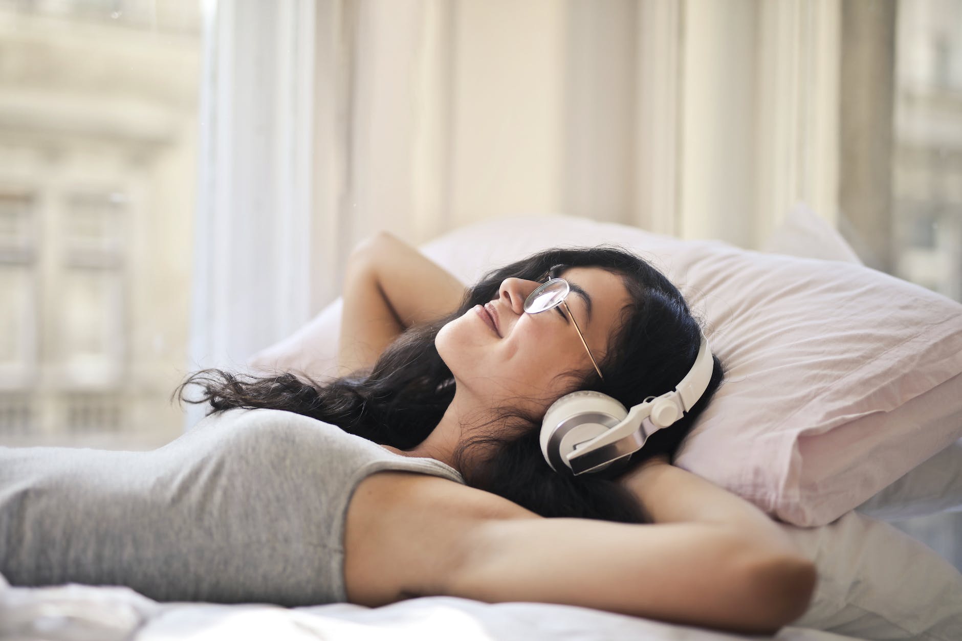 a lady lying on a bed with headphones on smiling with eyes closed