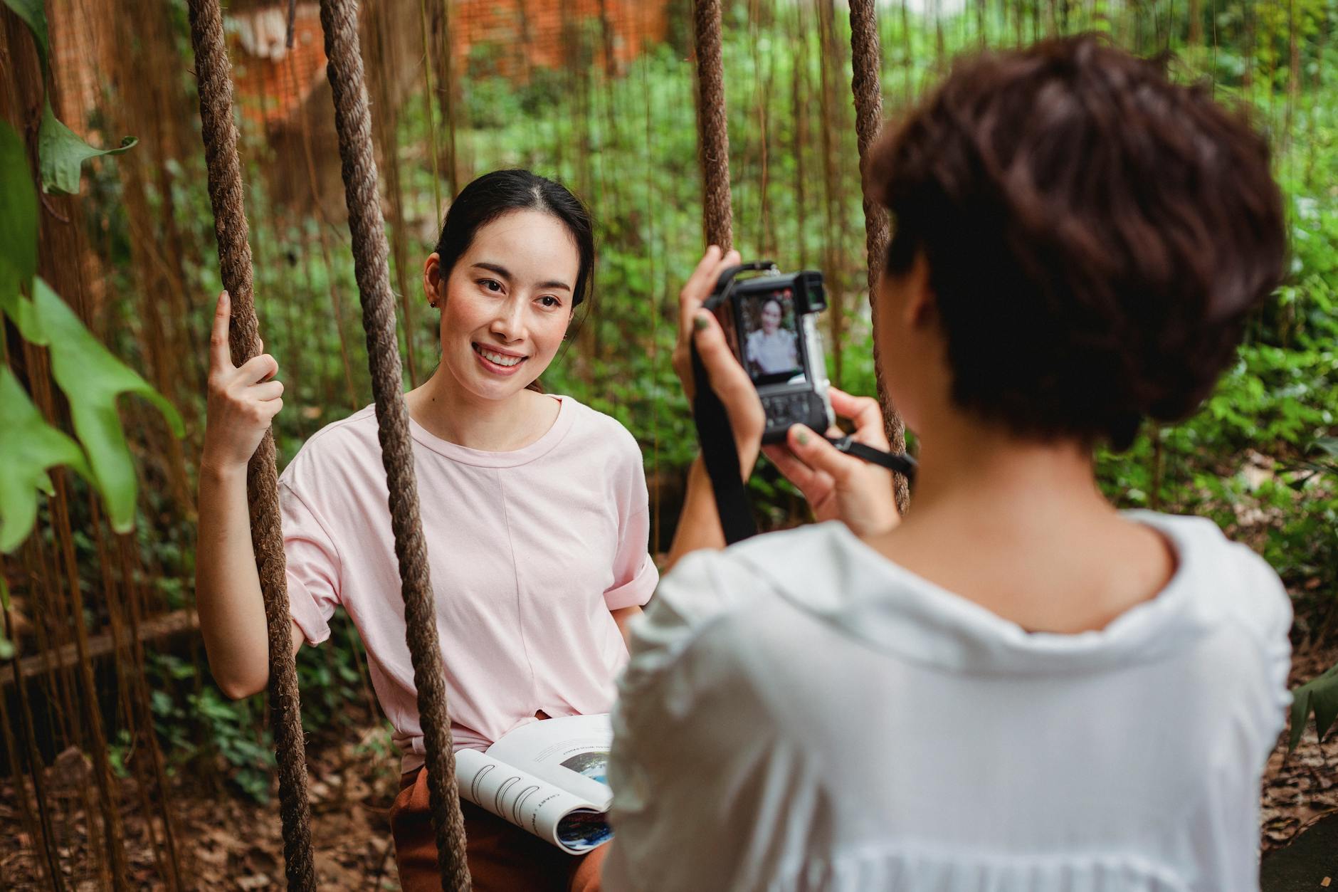 a lady taking a photo of a woman on a tree swing