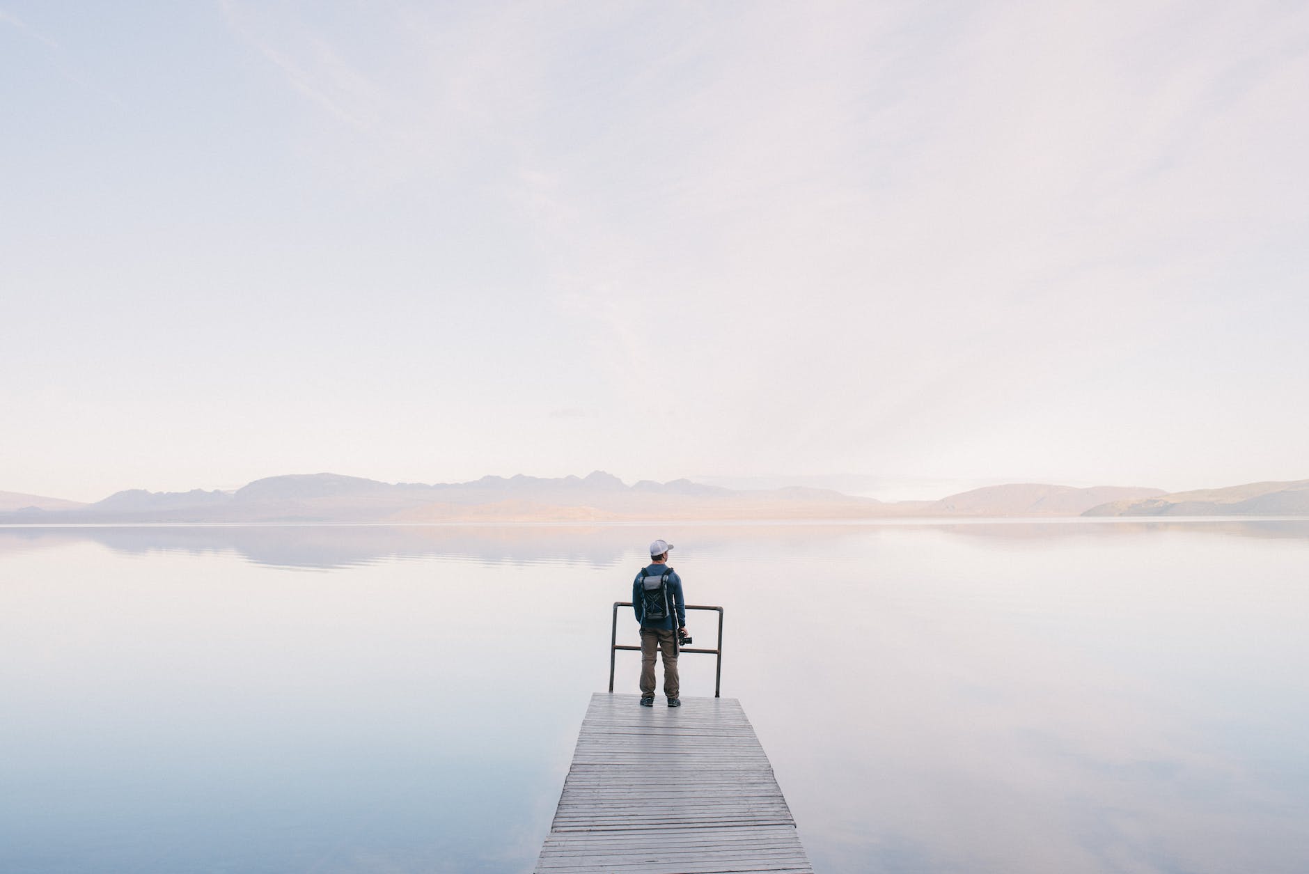 a photographer stood on  the end of a pier overlooking a lake on a misty morning