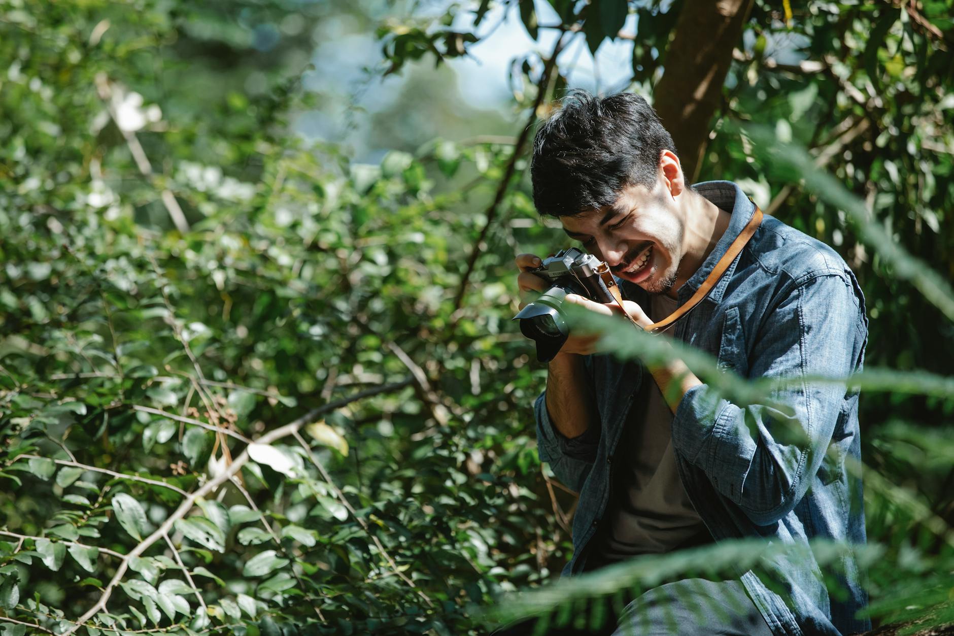 a man with a camera taking a photo in the woods smiling