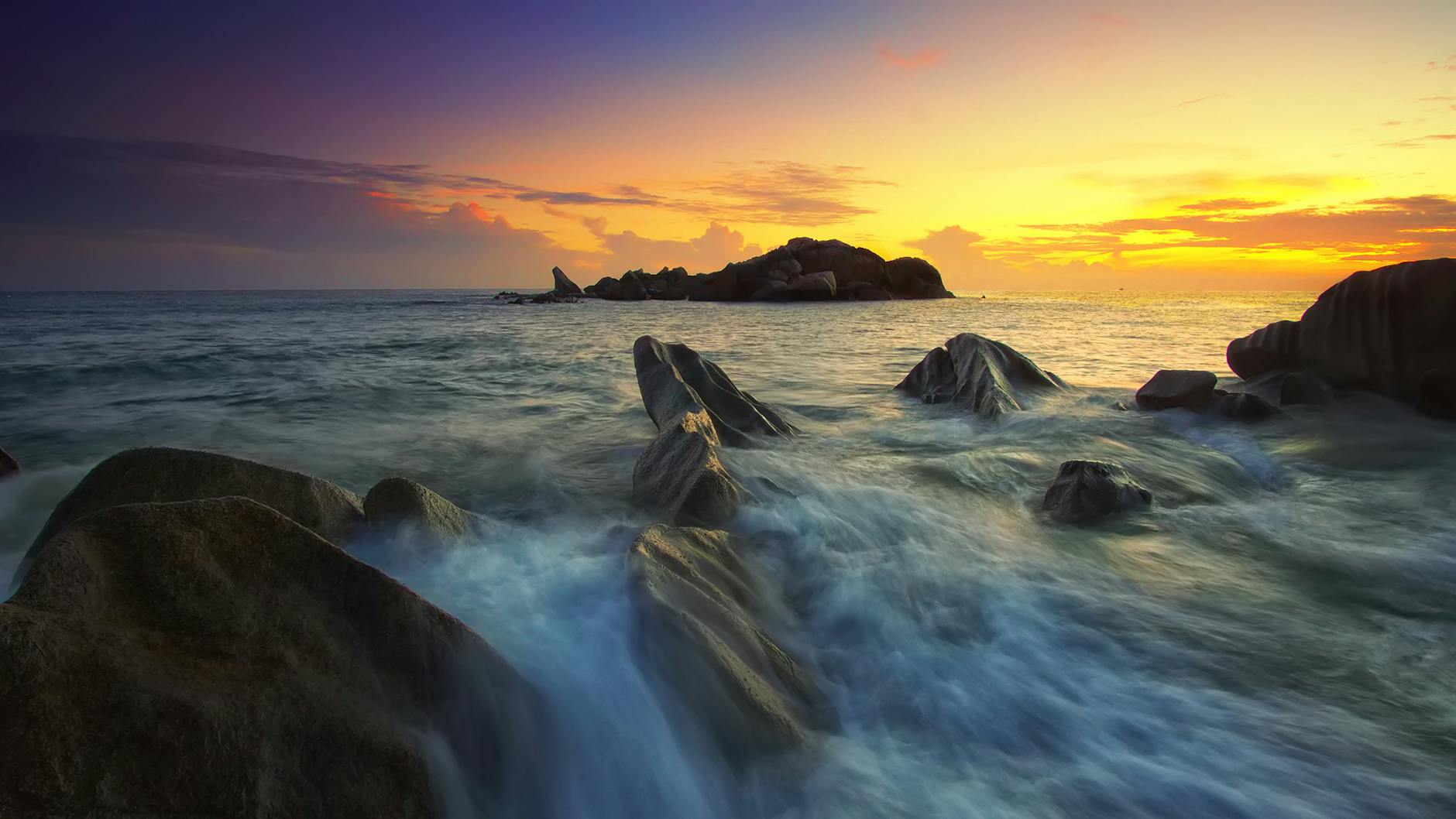 The sea rushing over the rocks onto the shore at a beach during sunset