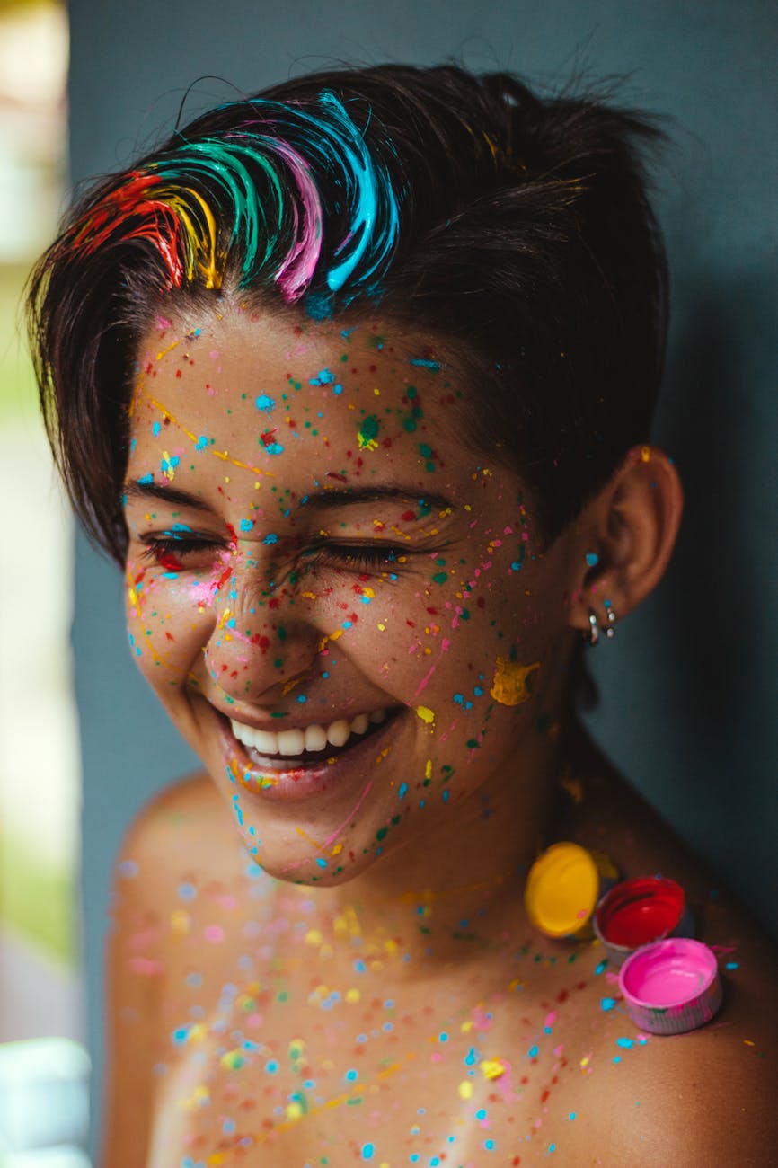 a lady with colour in her hair and paint splashes on her face smiling