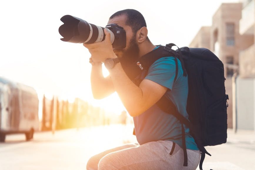 man carrying backpack taking photo using dslr camera